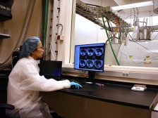 A woman sits at a computer in front of a window overlooking an MRI